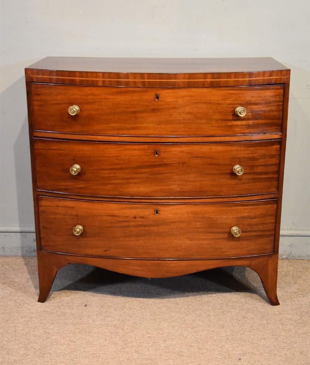 A Regency period mahogany bow-fronted chest featuring three full-width drawers with brass handles and splayed bracket feet. View II