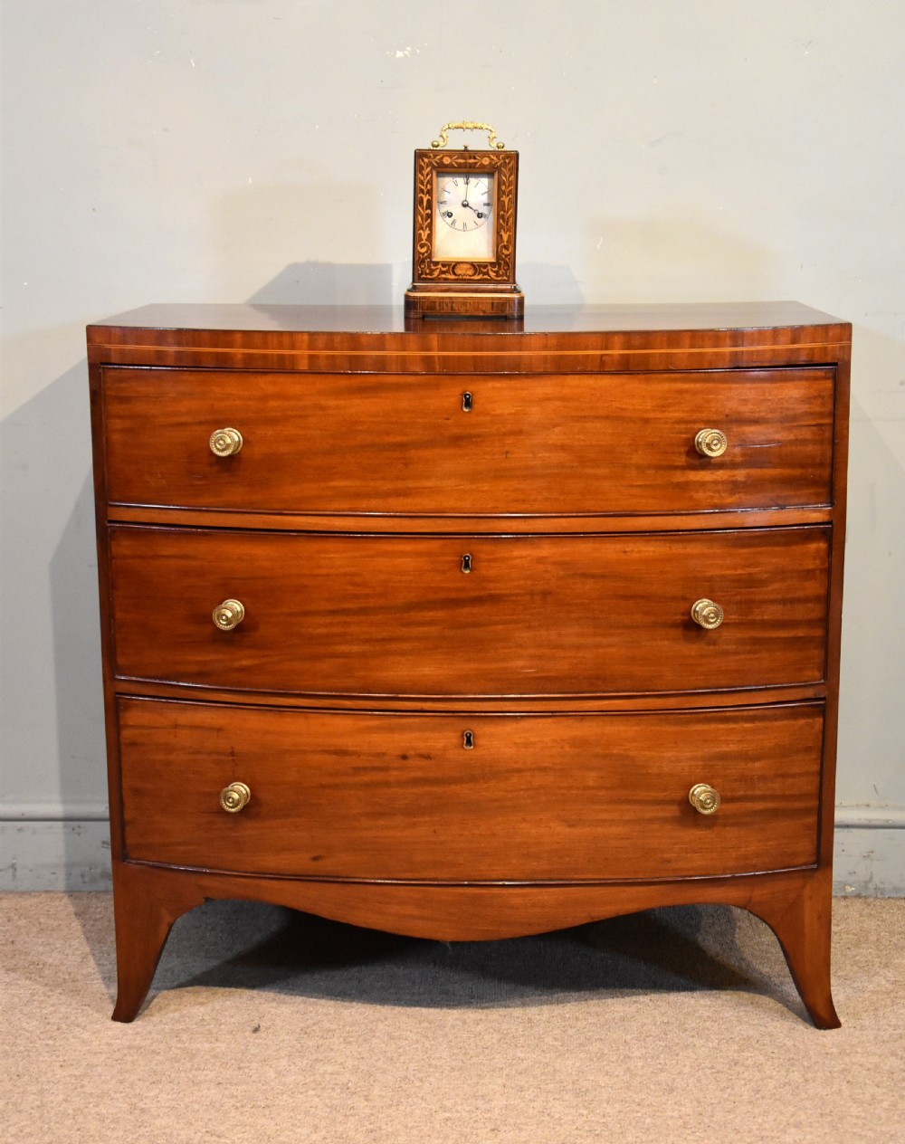 A Regency period mahogany bow-fronted chest featuring three full-width drawers with brass handles and splayed bracket feet. View III