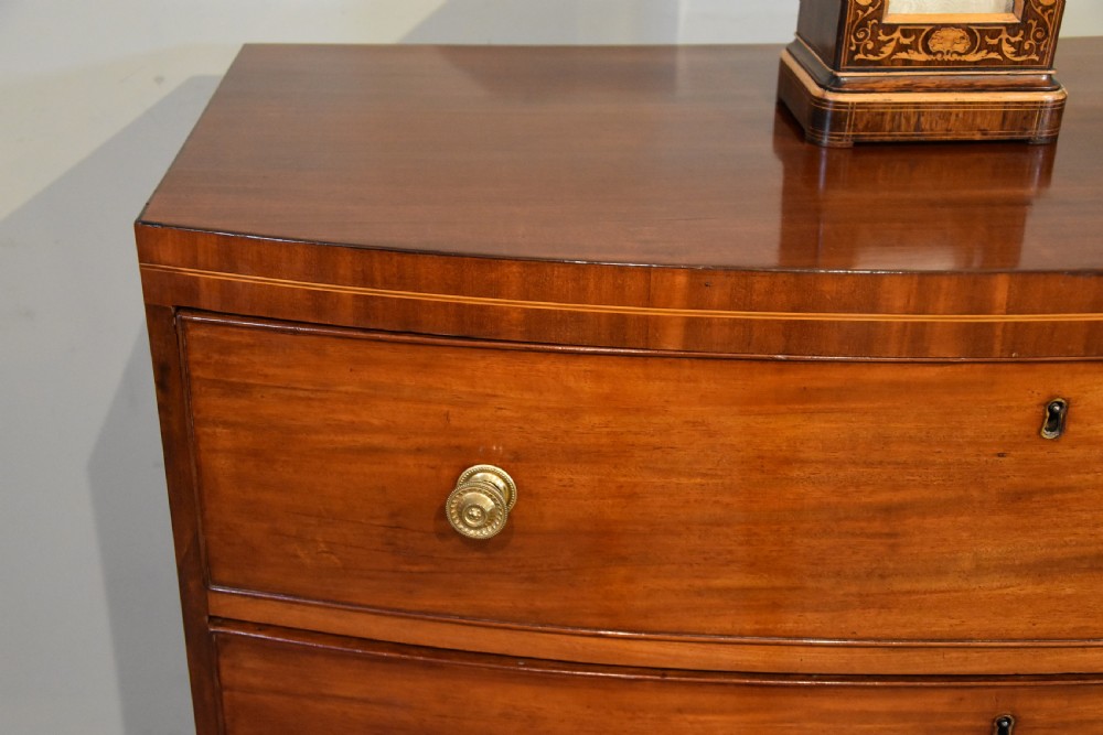 A Regency period mahogany bow-fronted chest featuring three full-width drawers with brass handles and splayed bracket feet. View IV