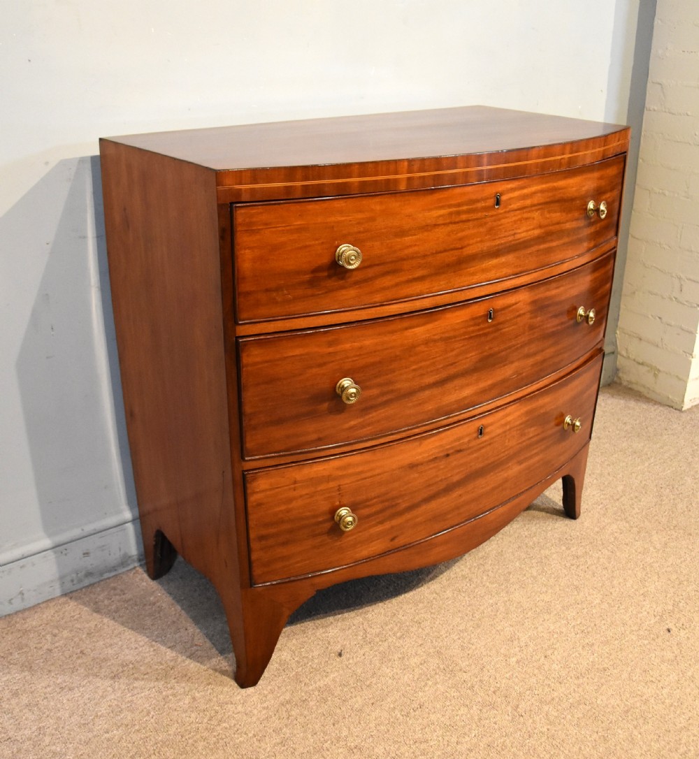 A Regency period mahogany bow-fronted chest featuring three full-width drawers with brass handles and splayed bracket feet. View VI