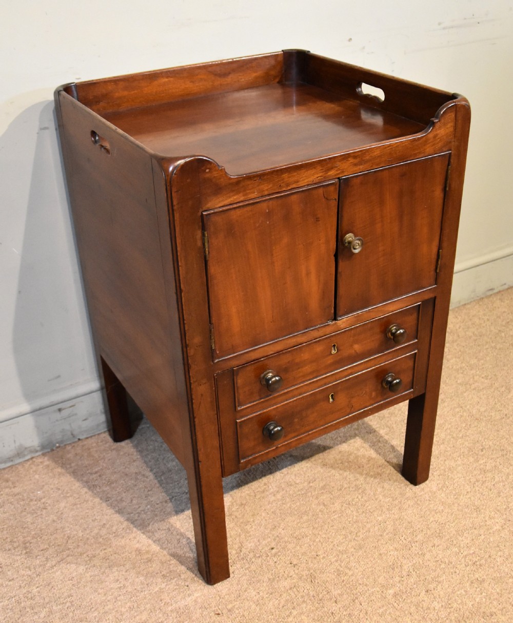 A George III mahogany bedside cabinet featuring a gallery tray top with pierced side handles, double cupboard doors, and two drawers below. View II