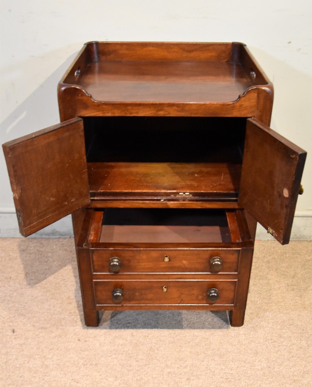 A George III mahogany bedside cabinet featuring a gallery tray top with pierced side handles, double cupboard doors, and two drawers below. View III