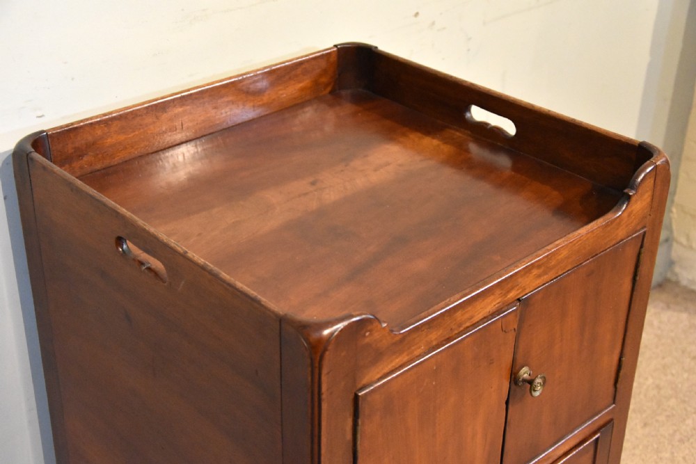 A George III mahogany bedside cabinet featuring a gallery tray top with pierced side handles, double cupboard doors, and two drawers below. View V