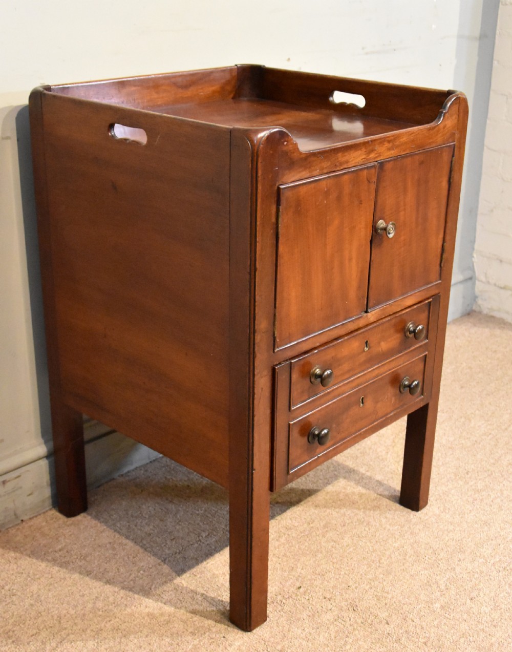 A George III mahogany bedside cabinet featuring a gallery tray top with pierced side handles, double cupboard doors, and two drawers below. View VI