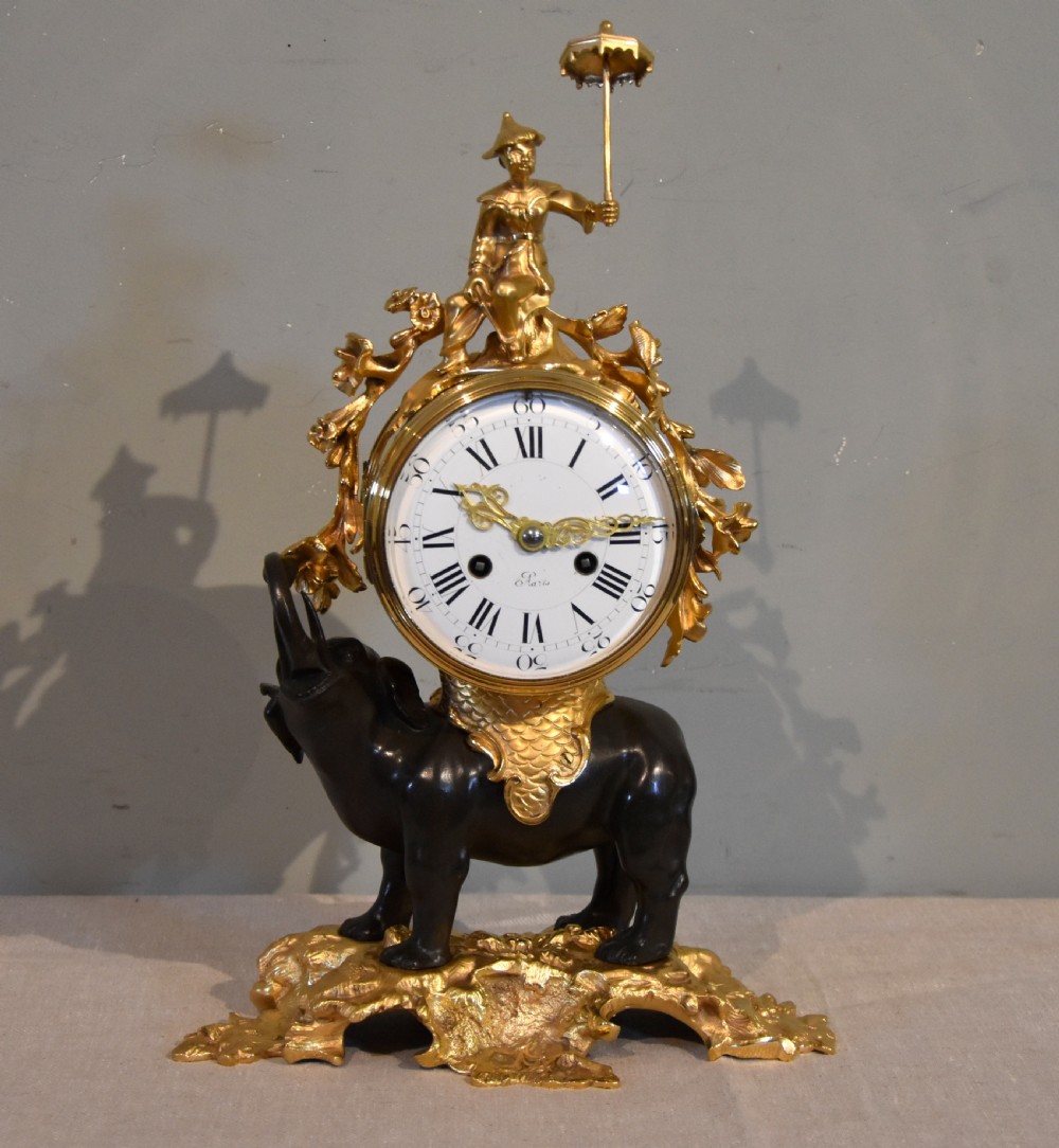 A French Louis XV style mantel clock featuring a dark patinated bronze elephant supporting an ormolu clock drum topped with a figure holding a parasol, mounted on a gilded rocaille base. View III