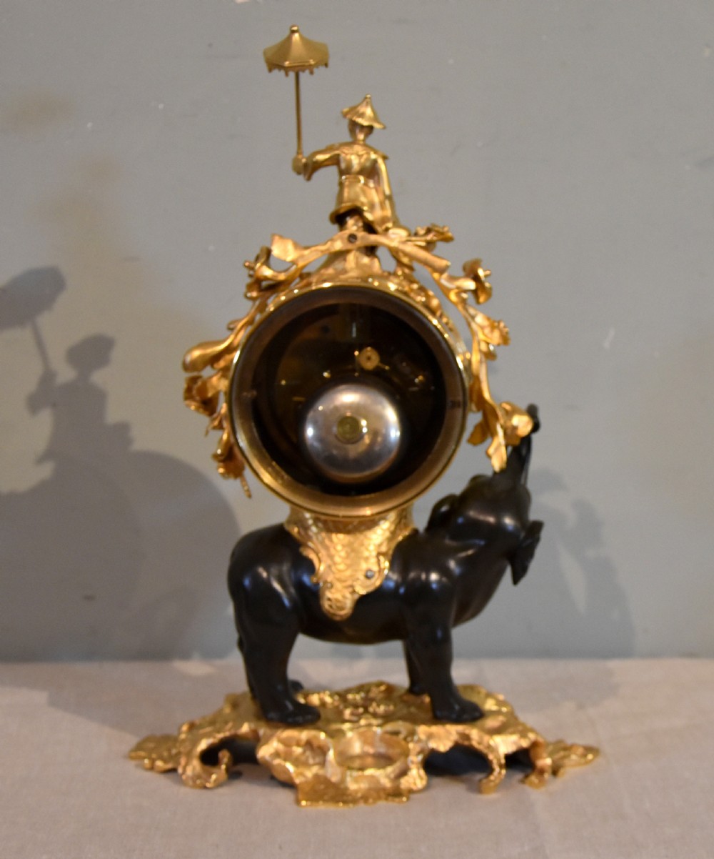 A French Louis XV style mantel clock featuring a dark patinated bronze elephant supporting an ormolu clock drum topped with a figure holding a parasol, mounted on a gilded rocaille base. View IV