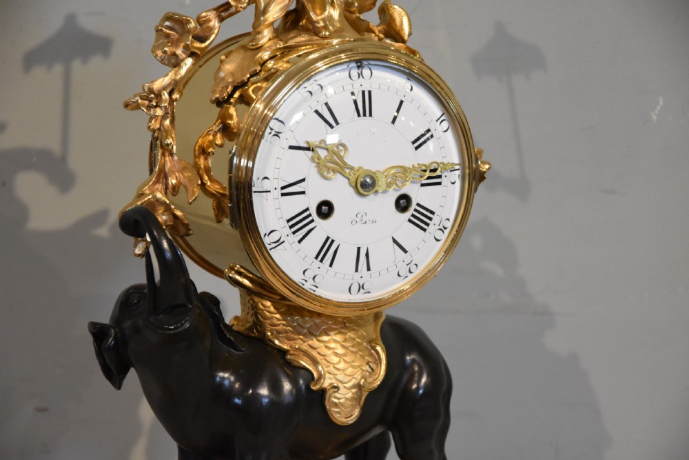 A French Louis XV style mantel clock featuring a dark patinated bronze elephant supporting an ormolu clock drum topped with a figure holding a parasol, mounted on a gilded rocaille base. View V