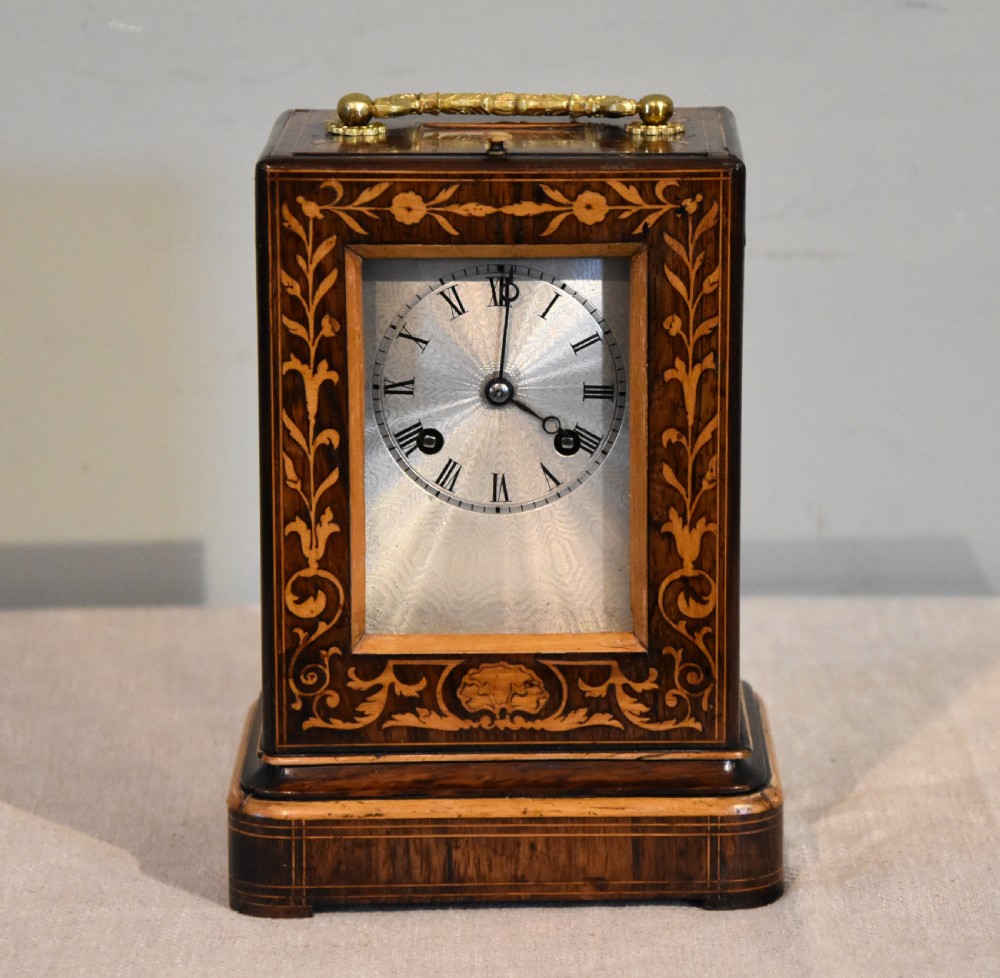 An antique French rectangular rosewood mantel clock featuring foliate marquetry inlay, a silvered engine-turned dial with Roman numerals, and a gilt brass handle.