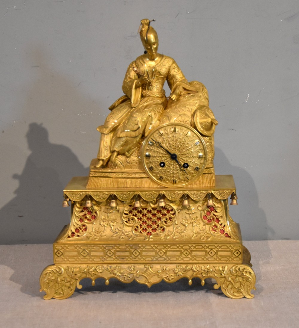 An antique French ormolu mantel clock featuring a sculpted Chinoiserie figure seated atop an intricate tiered base with suspended bells.