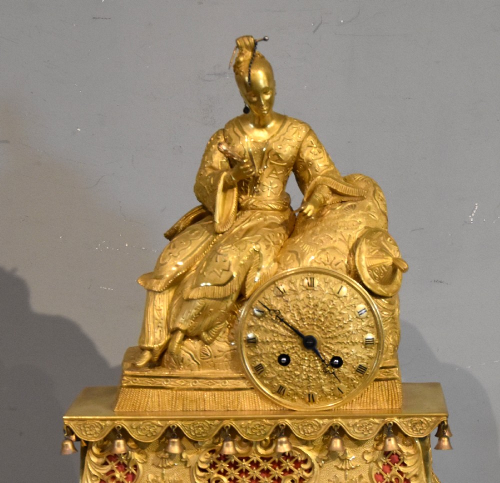 An antique French ormolu mantel clock featuring a sculpted Chinoiserie figure seated atop an intricate tiered base with suspended bells. View II