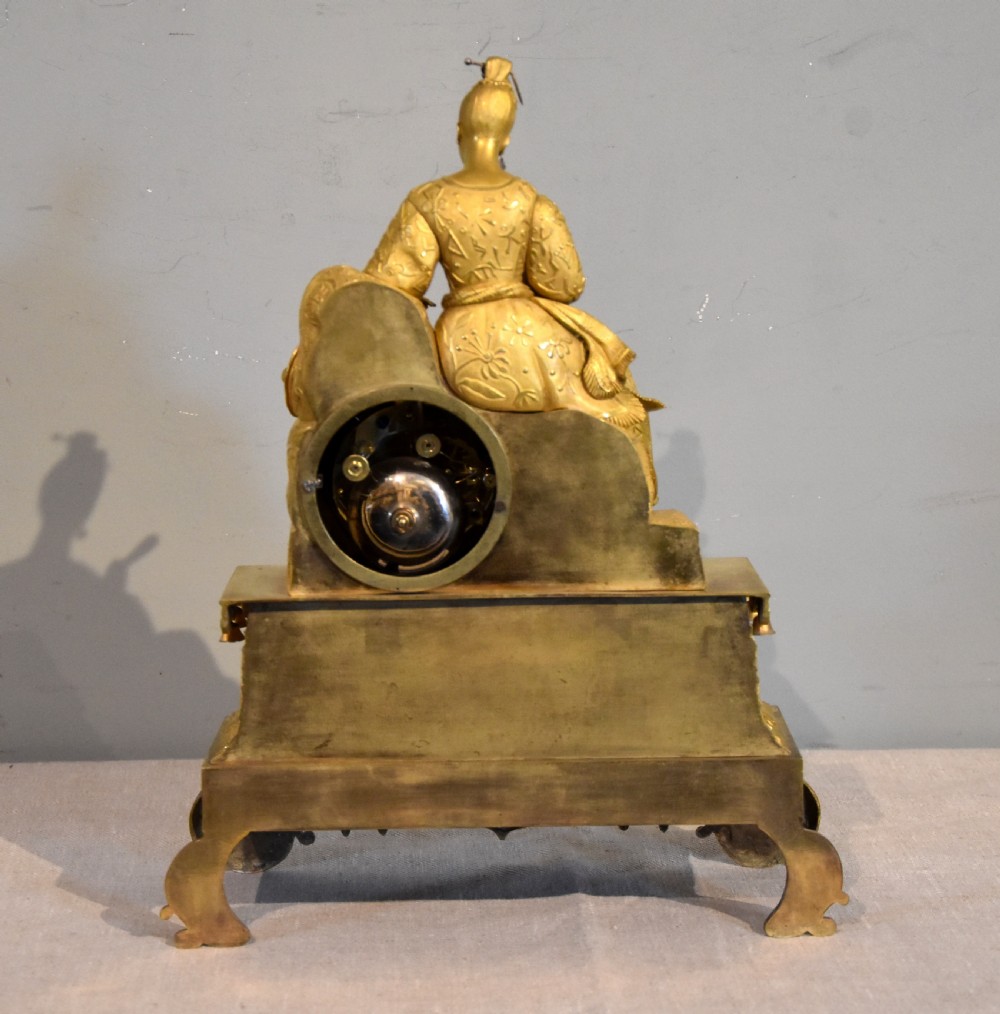 An antique French ormolu mantel clock featuring a sculpted Chinoiserie figure seated atop an intricate tiered base with suspended bells. View IV