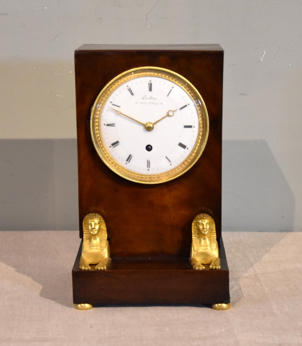 A French Empire mahogany mantel clock featuring a white dial with Roman numerals, gilt bronze beaded bezel, and two gold sphinx mounts on a stepped base.