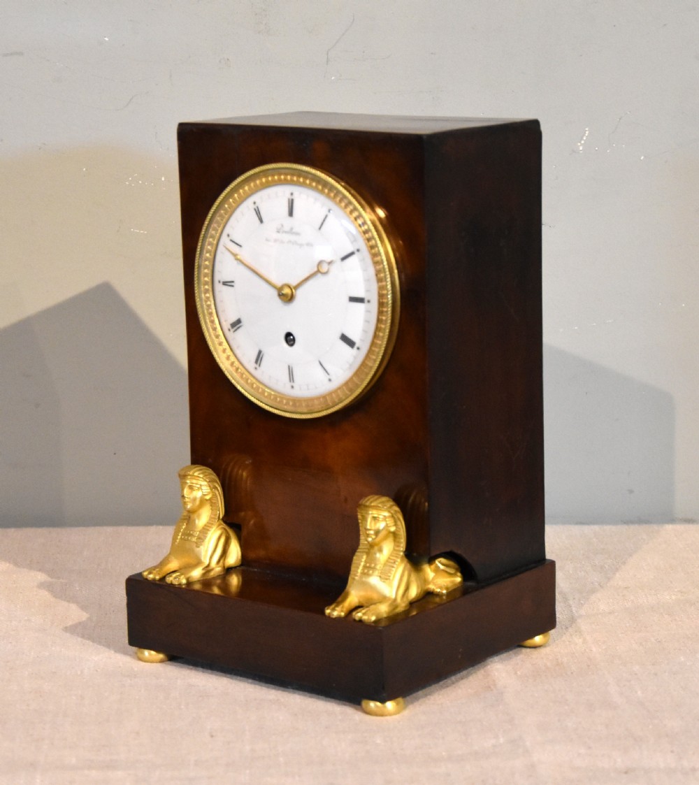 A French Empire mahogany mantel clock featuring a white dial with Roman numerals, gilt bronze beaded bezel, and two gold sphinx mounts on a stepped base. View II