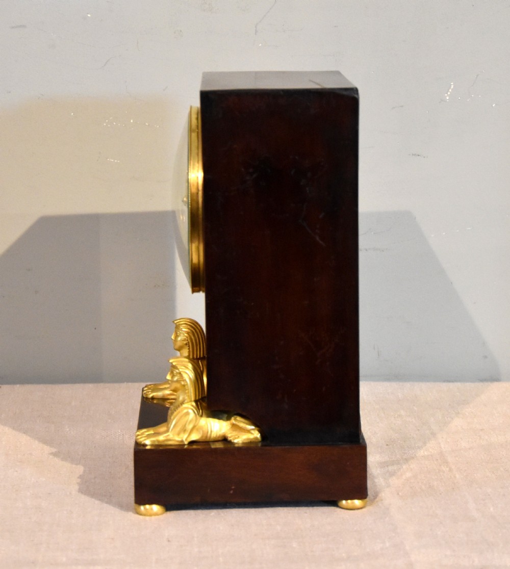 A French Empire mahogany mantel clock featuring a white dial with Roman numerals, gilt bronze beaded bezel, and two gold sphinx mounts on a stepped base. View III