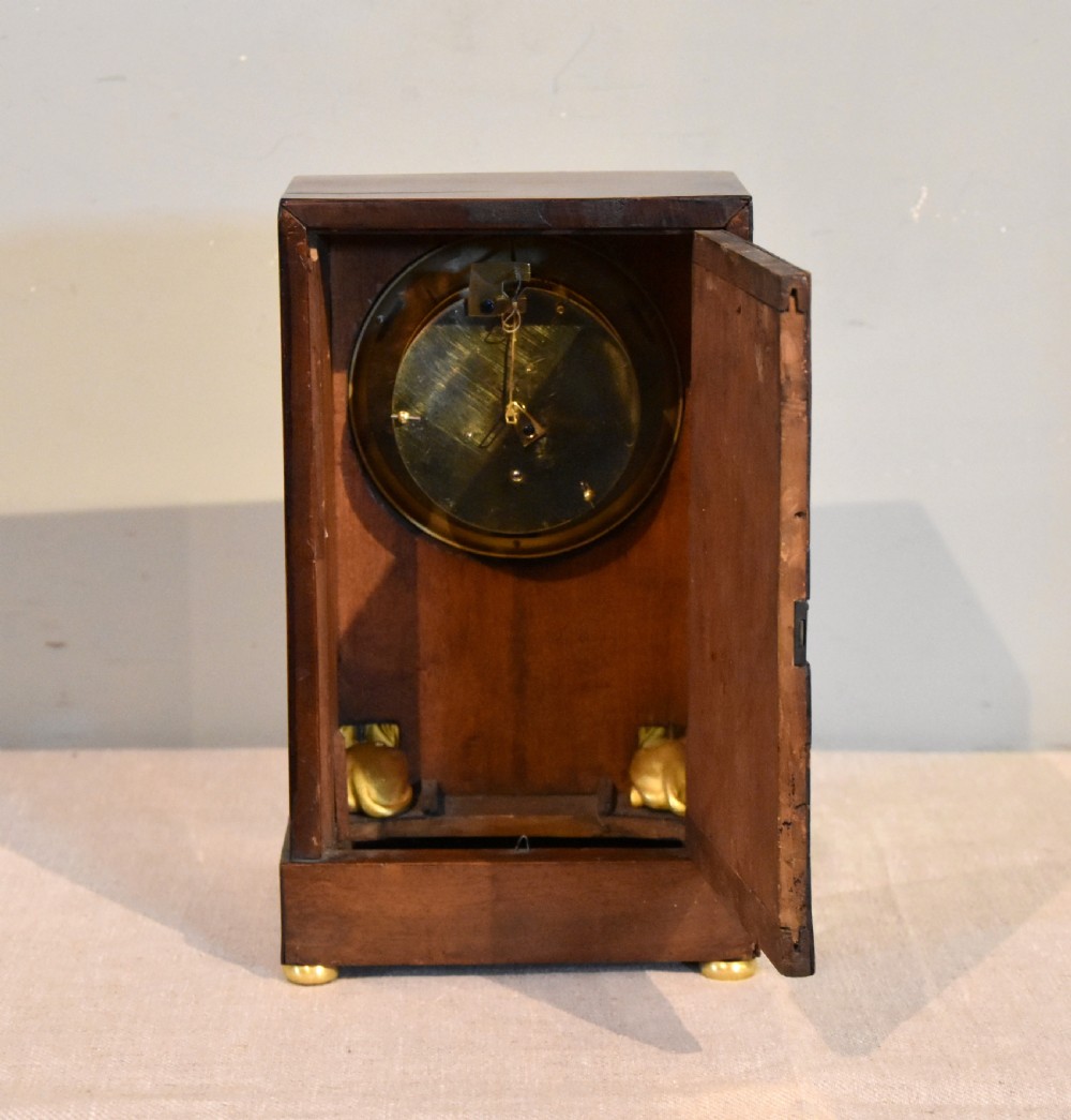 A French Empire mahogany mantel clock featuring a white dial with Roman numerals, gilt bronze beaded bezel, and two gold sphinx mounts on a stepped base. View IV