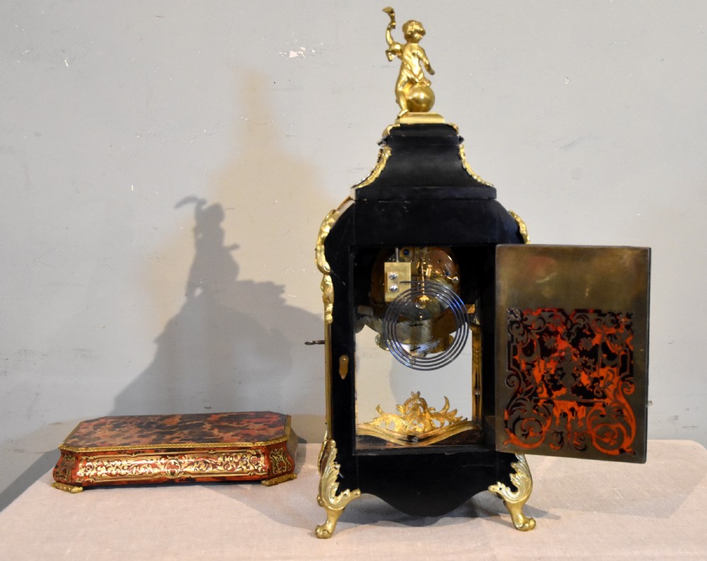 An ornate Boulle work mantel clock featuring red tortoiseshell and brass marquetry, topped with a gilt bronze cherub figure and set with blue enamel Roman numeral cartouches. View IV