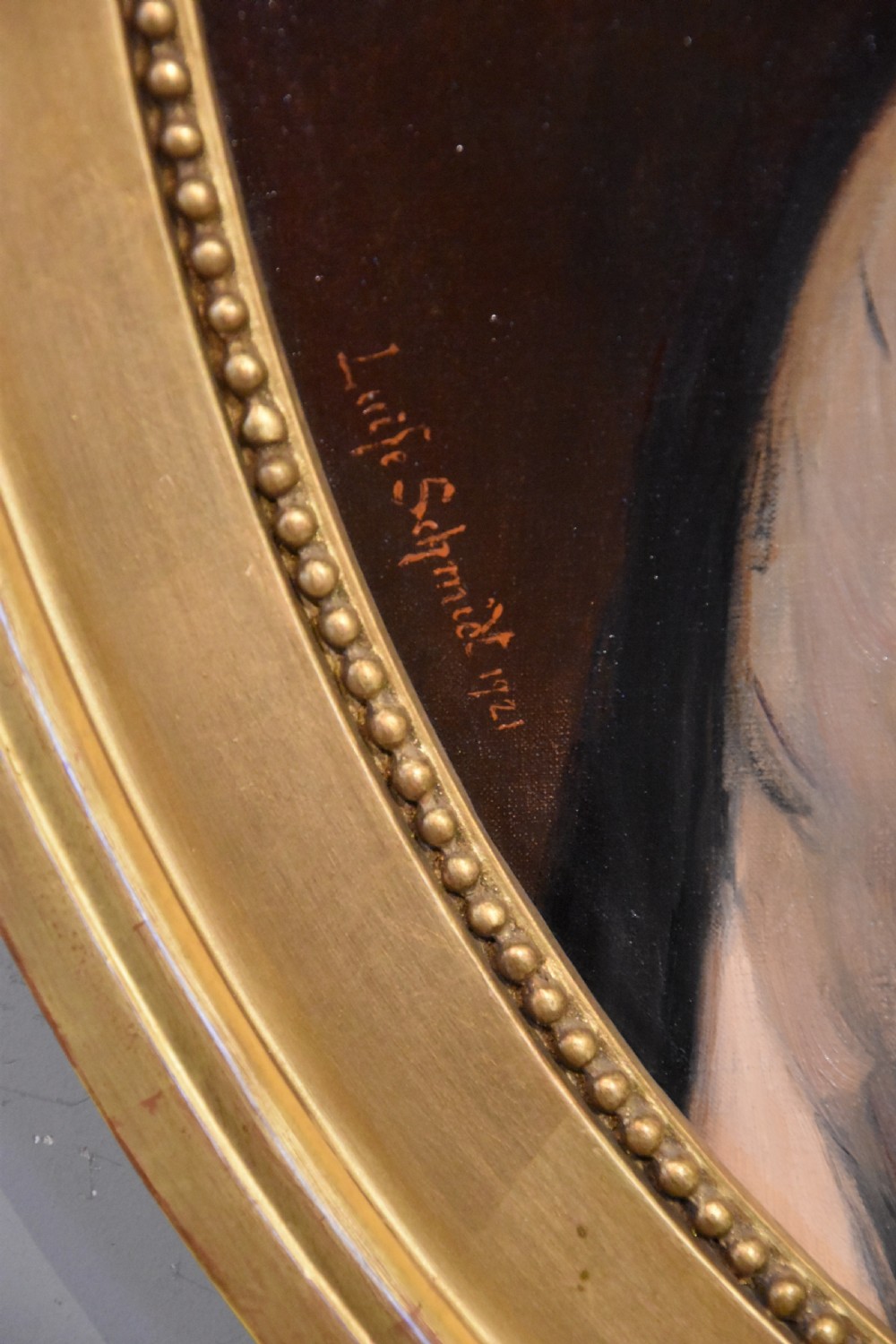 An oval antique oil painting featuring a seated lady in a black gown with a red rose corsage, set within a carved giltwood frame with a ribbon cresting. View III