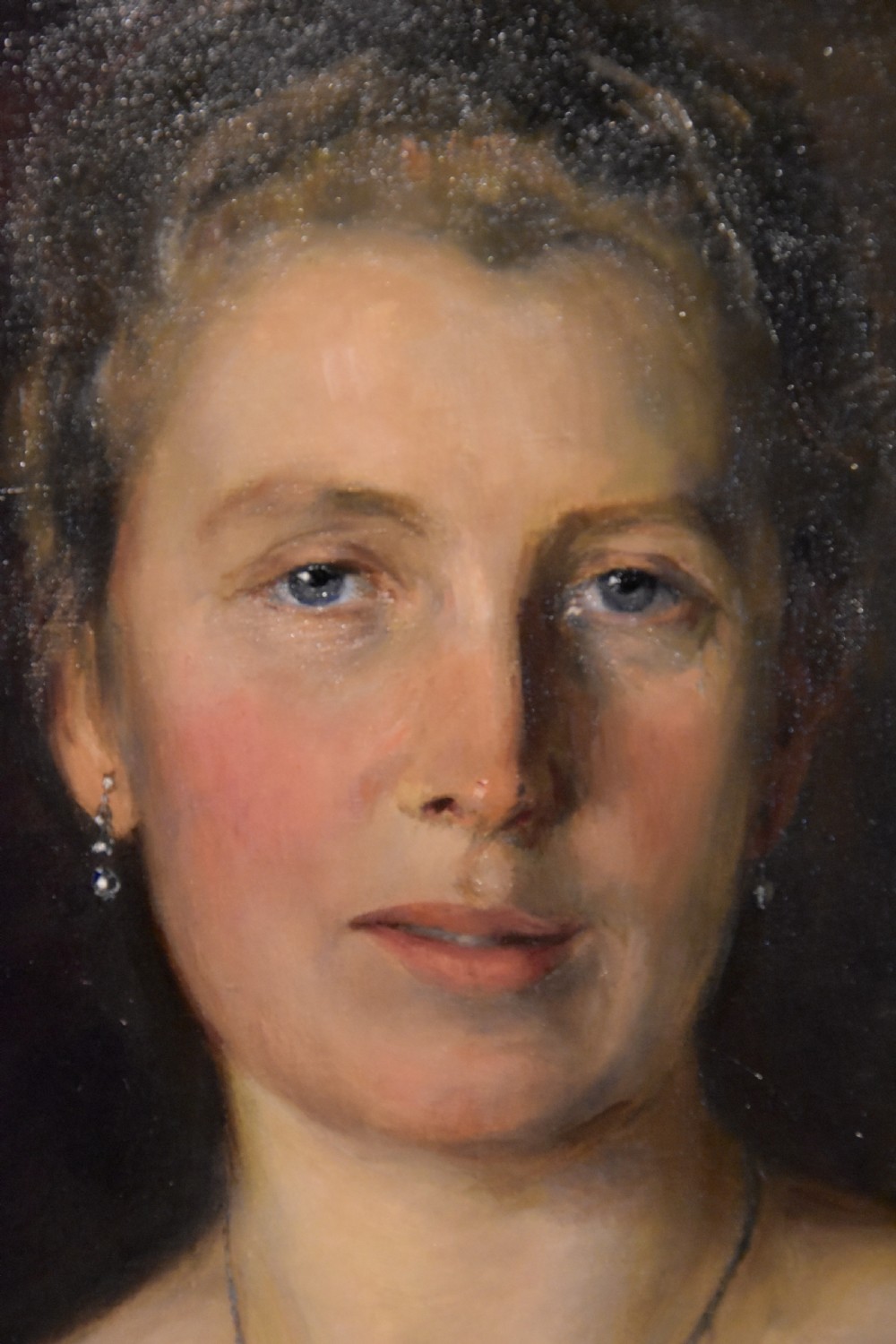 An oval antique oil painting featuring a seated lady in a black gown with a red rose corsage, set within a carved giltwood frame with a ribbon cresting. View IV