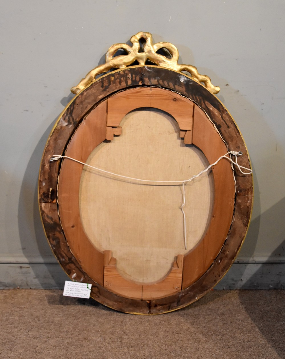 An oval antique oil painting featuring a seated lady in a black gown with a red rose corsage, set within a carved giltwood frame with a ribbon cresting. View V