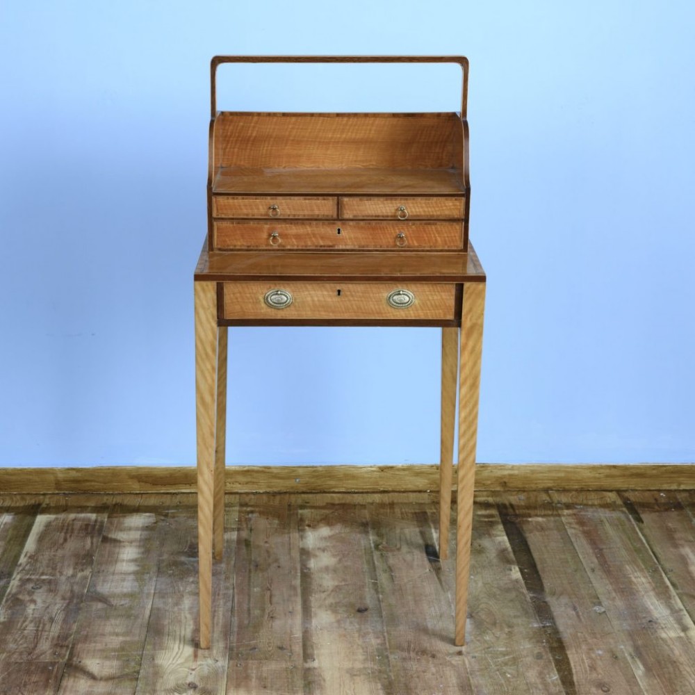 An 18th-century Georgian satinwood cheveret writing table featuring slender tapered legs, a lower drawer, and an upper removable book trough with handle.