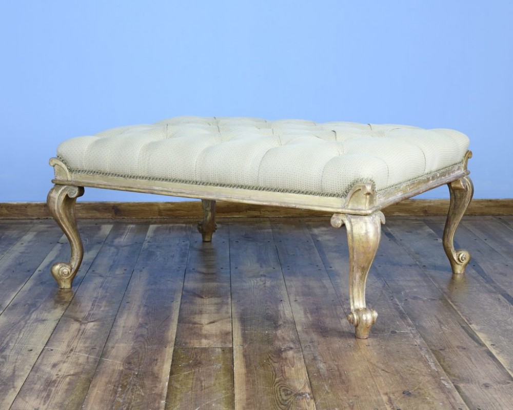 A large square William IV parcel gilt footstool featuring deep-buttoned cream upholstery and carved cabriole legs.