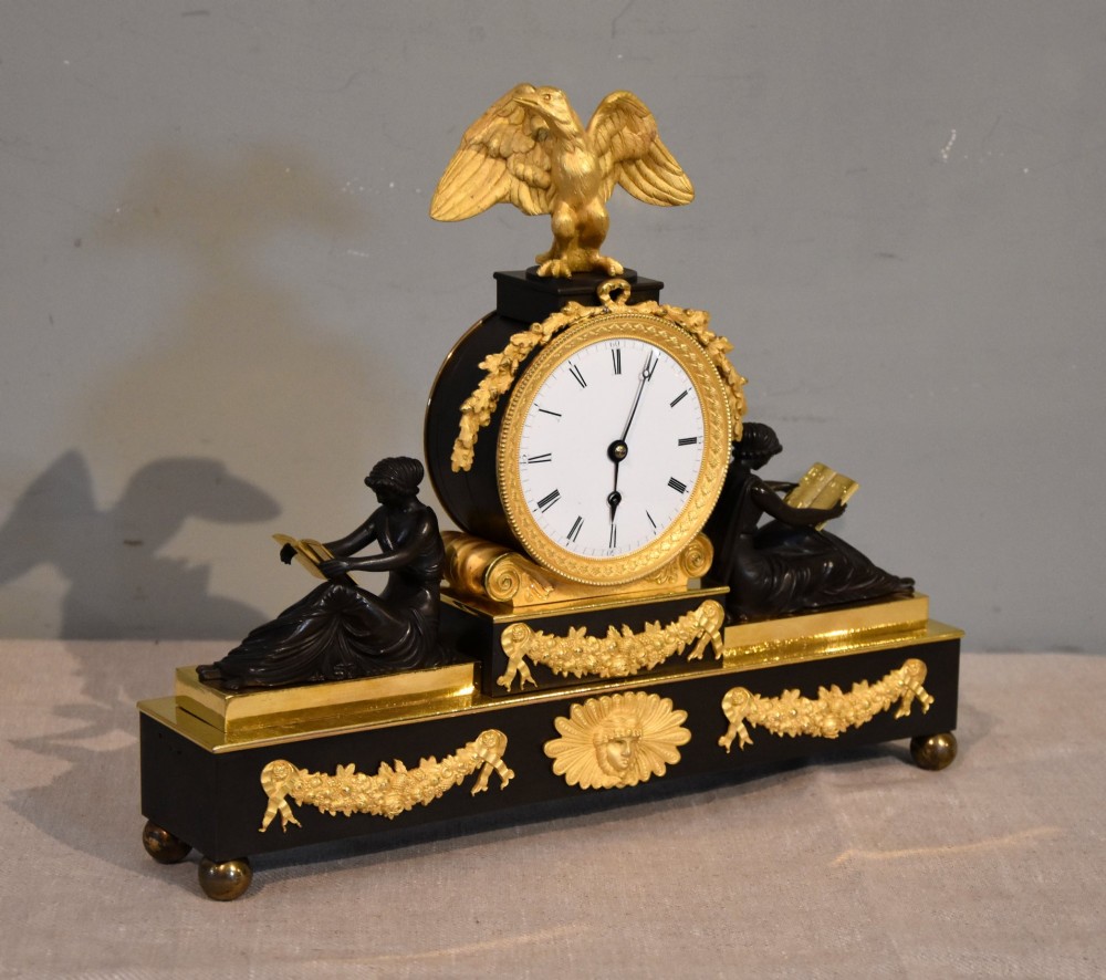 An English Regency gilt brass and patinated bronze mantel timepiece featuring a top eagle finial, circular enamel dial, and two seated classical female figures. View II