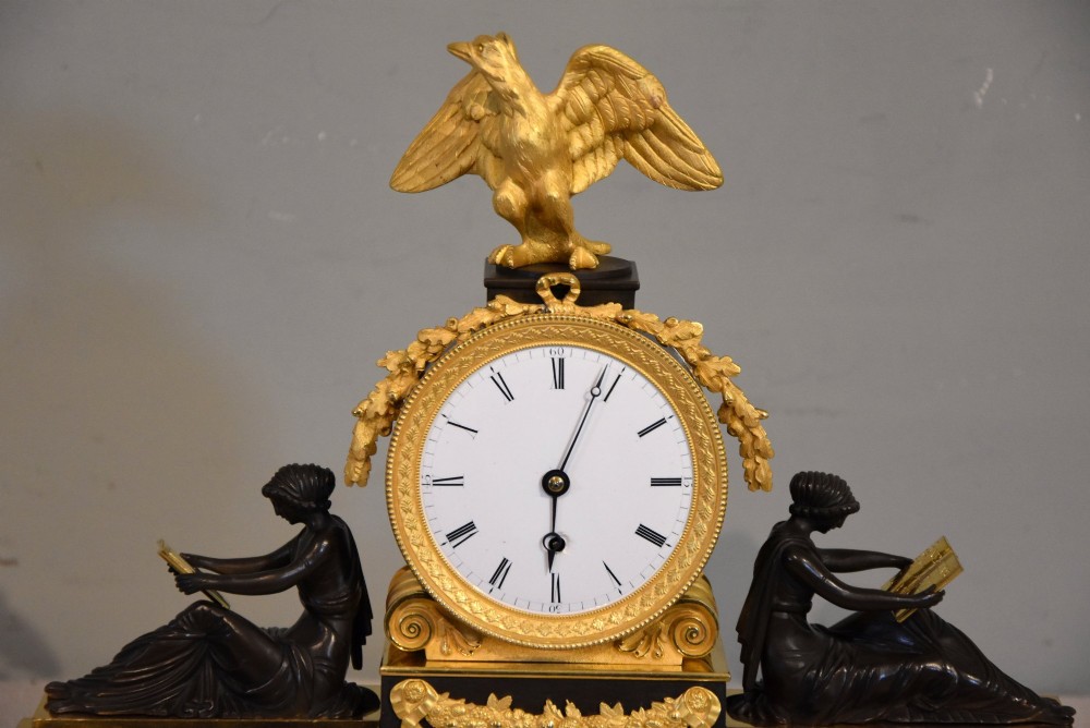 An English Regency gilt brass and patinated bronze mantel timepiece featuring a top eagle finial, circular enamel dial, and two seated classical female figures. View III