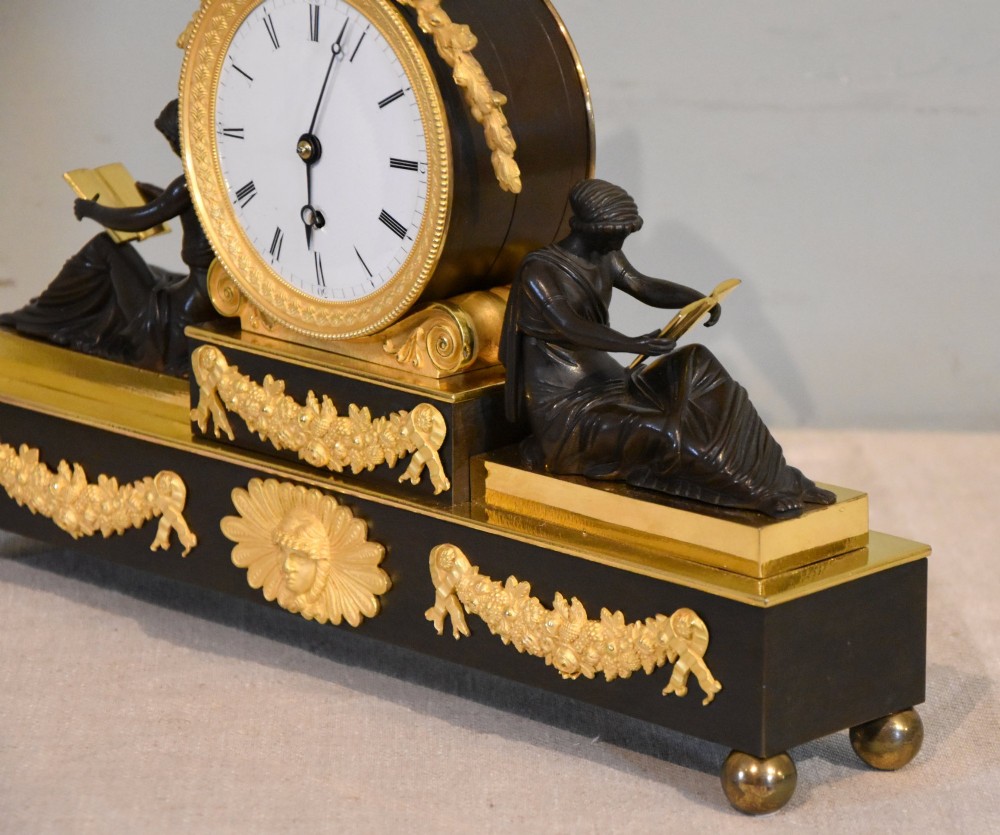An English Regency gilt brass and patinated bronze mantel timepiece featuring a top eagle finial, circular enamel dial, and two seated classical female figures. View IV