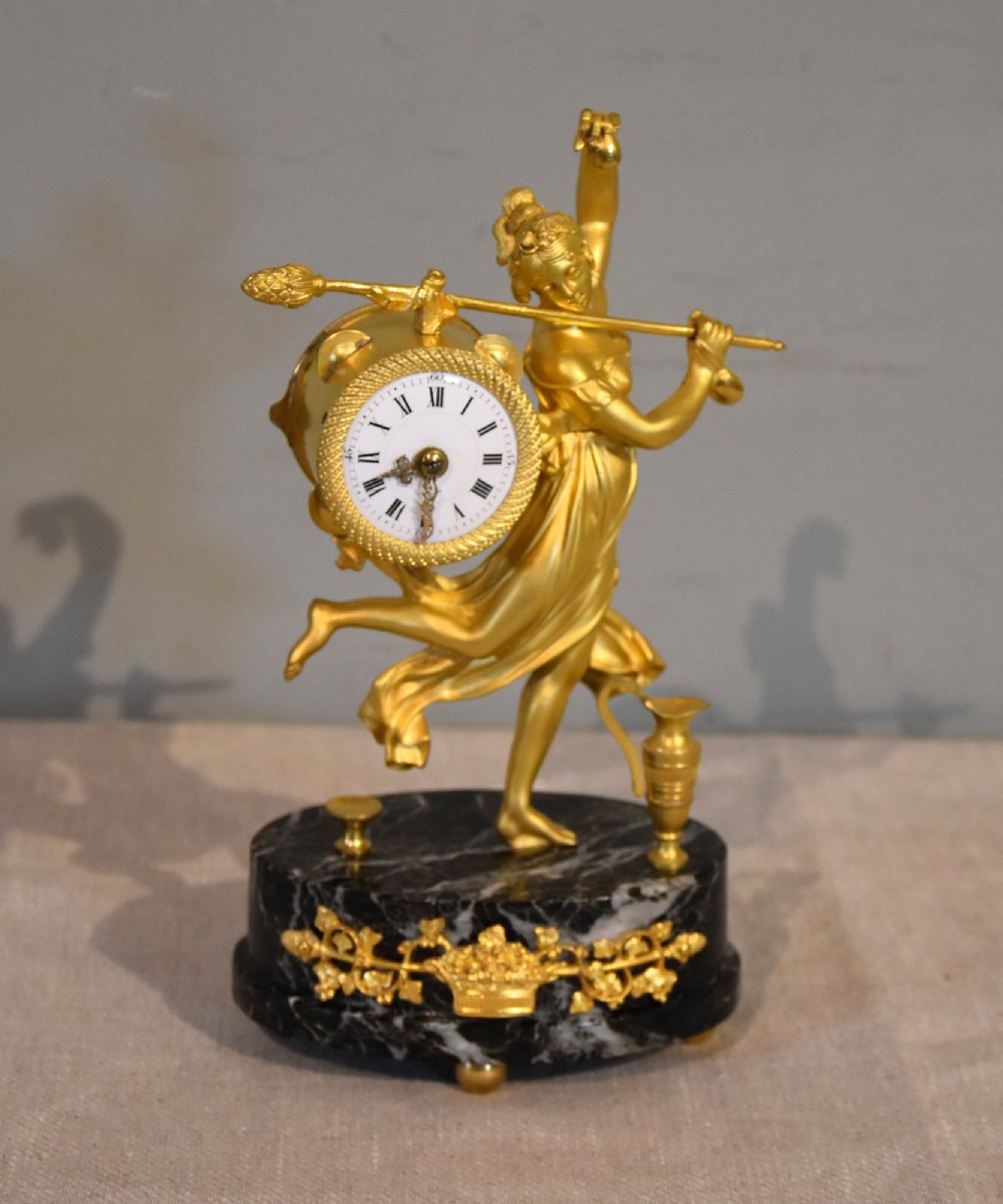 A French 19th-century gilt bronze figural mantel clock depicting a classical dancing figure holding a tambourine clock face upon a dark marble base.