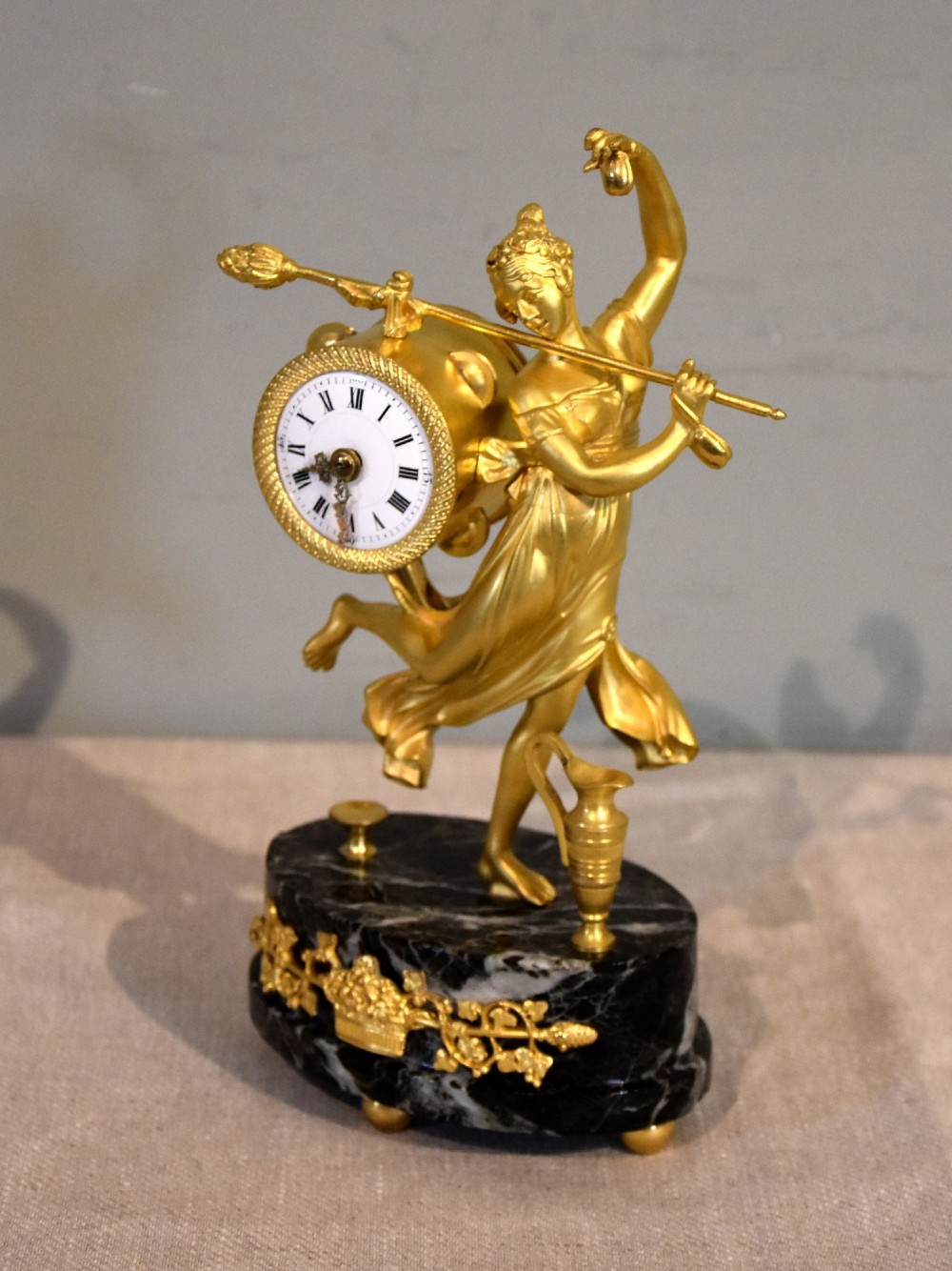 A French 19th-century gilt bronze figural mantel clock depicting a classical dancing figure holding a tambourine clock face upon a dark marble base. View II