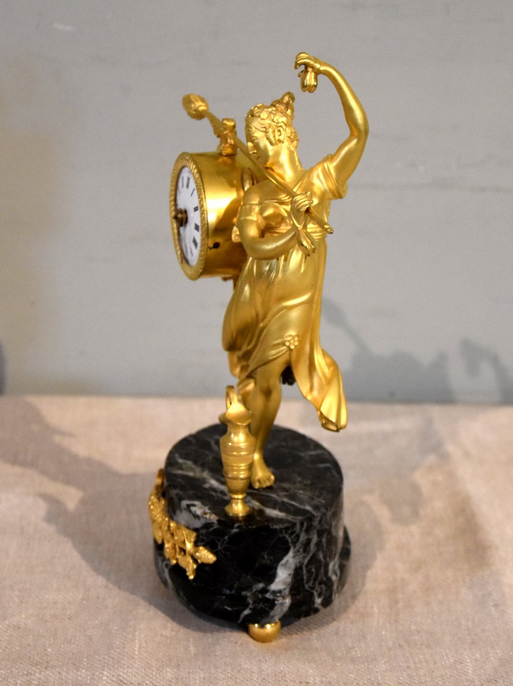 A French 19th-century gilt bronze figural mantel clock depicting a classical dancing figure holding a tambourine clock face upon a dark marble base. View III