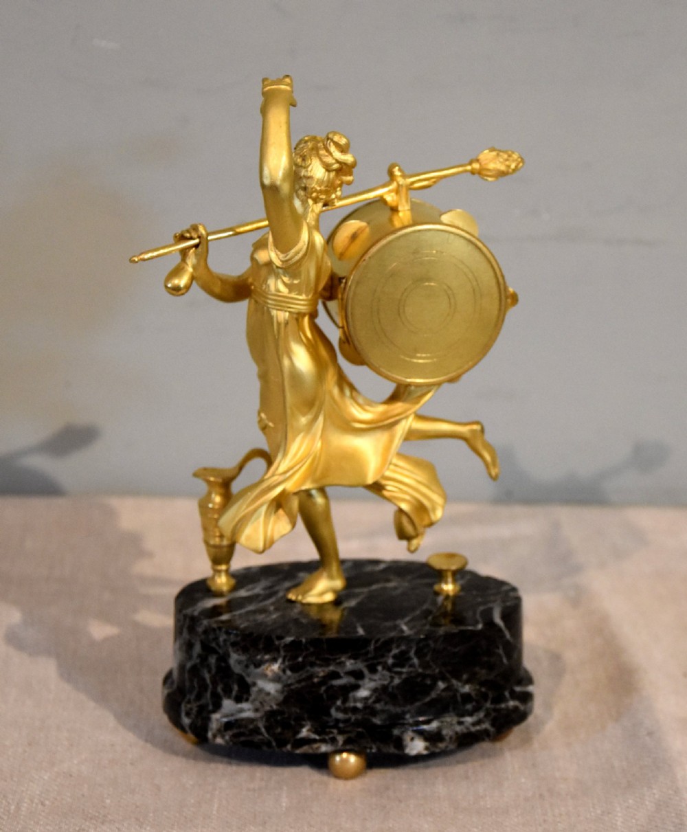 A French 19th-century gilt bronze figural mantel clock depicting a classical dancing figure holding a tambourine clock face upon a dark marble base. View IV