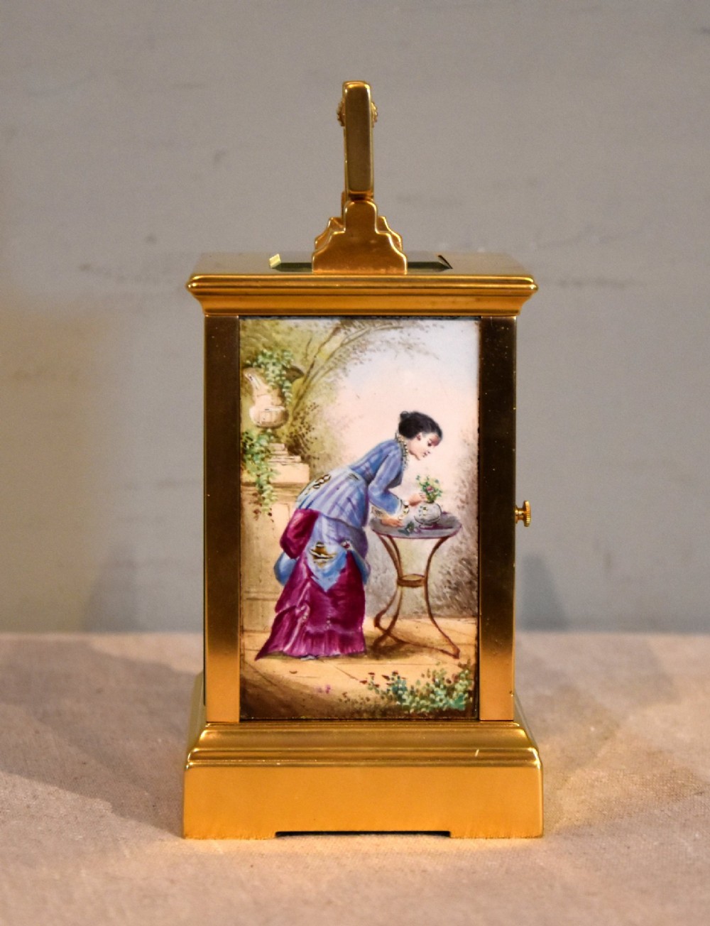 A gilt brass carriage clock featuring a rectangular case, a geometric top handle, and a hand-painted porcelain front panel illustrating a romantic couple in a landscape. View III