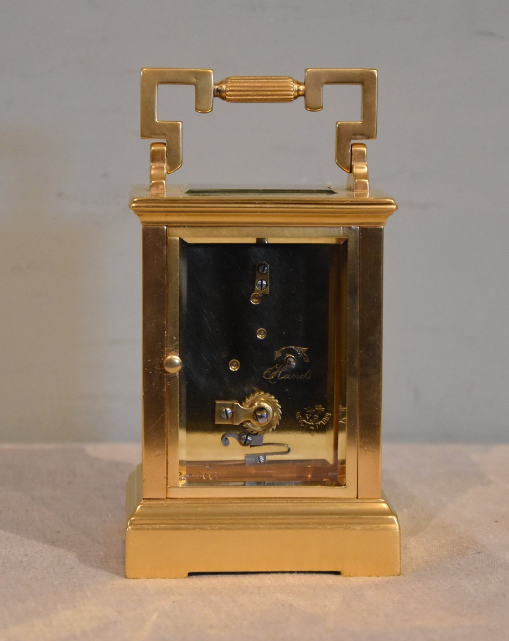 A gilt brass carriage clock featuring a rectangular case, a geometric top handle, and a hand-painted porcelain front panel illustrating a romantic couple in a landscape. View IV