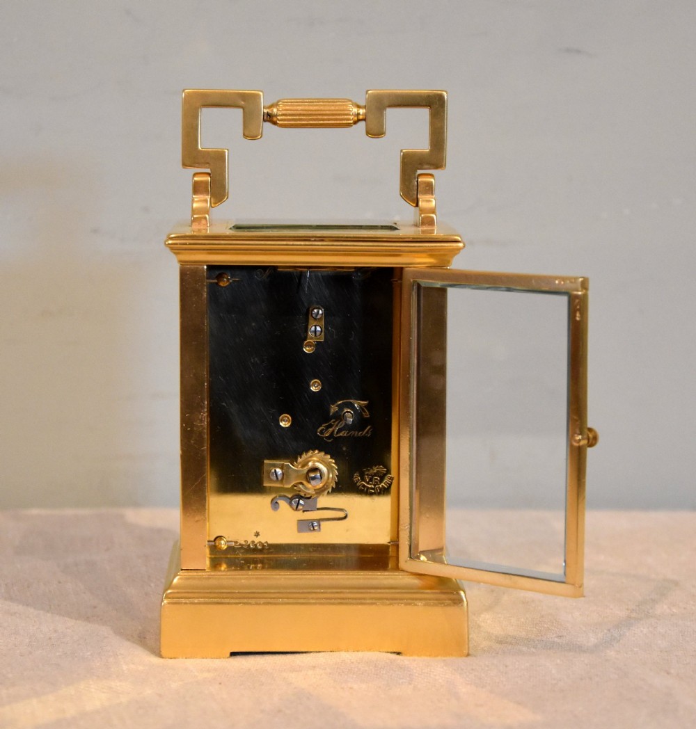 A gilt brass carriage clock featuring a rectangular case, a geometric top handle, and a hand-painted porcelain front panel illustrating a romantic couple in a landscape. View V