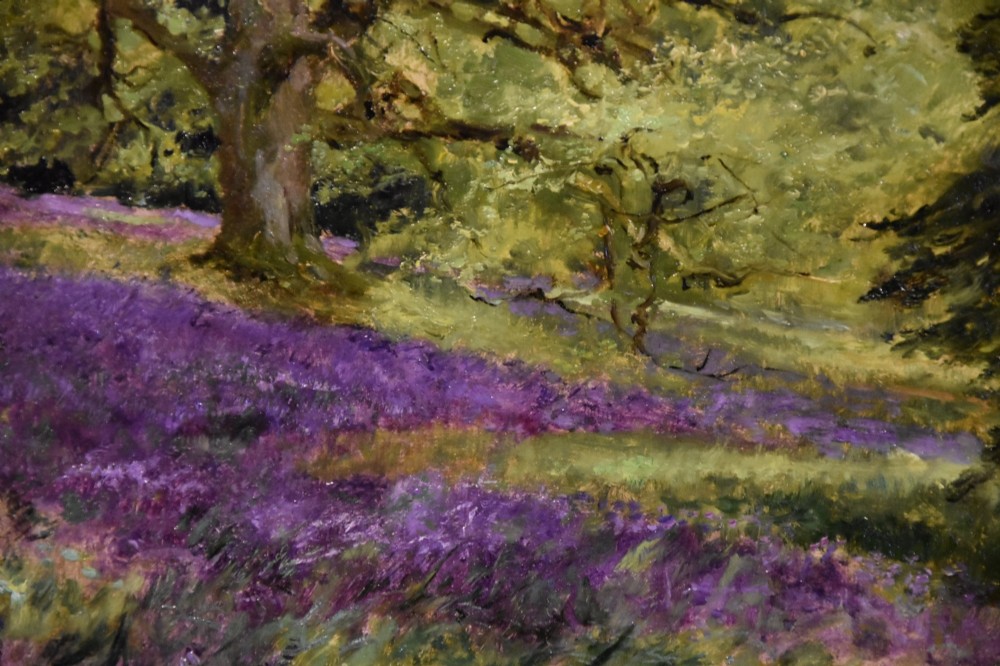 An antique oil painting depicting a woodland landscape with purple flowers beneath a tree, displayed within an ornate gilt frame. View III