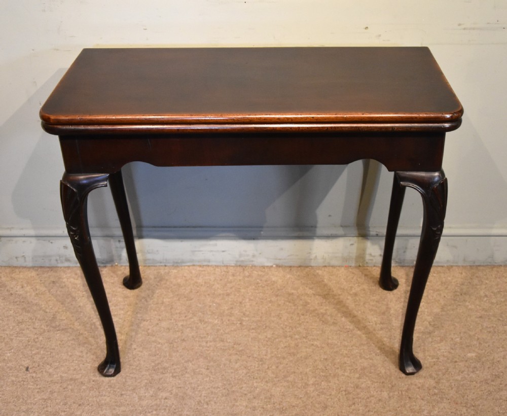 A dark mahogany George III fold-over card table resting on four slender carved cabriole legs with pad feet.