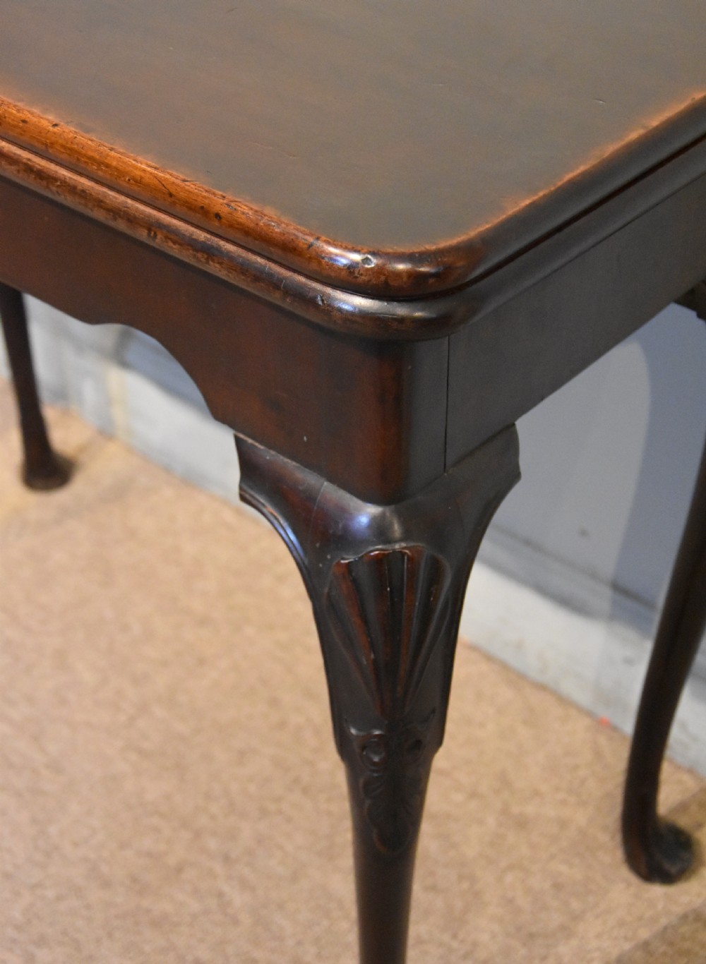 A dark mahogany George III fold-over card table resting on four slender carved cabriole legs with pad feet. View IV