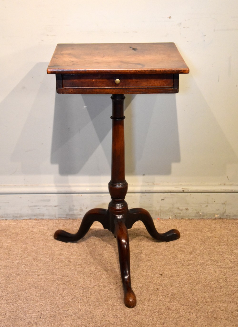 Mid-18th-century mahogany wine table featuring a rectangular top with a small drawer, supported by a turned central stem and three cabriole legs.