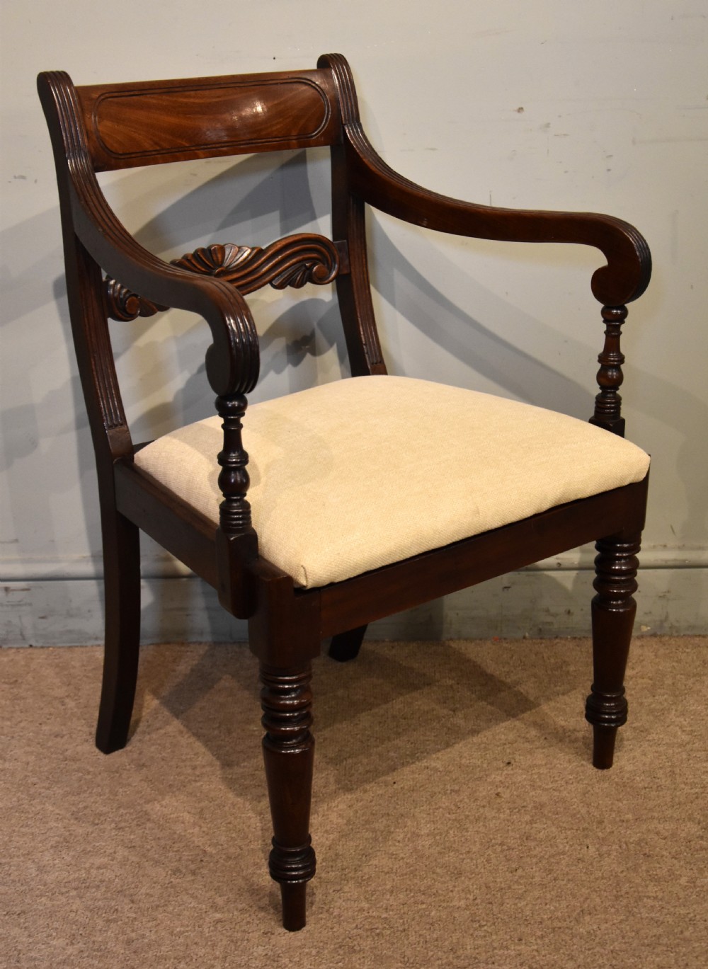 A Regency period mahogany open armchair featuring a reeded tablet top rail, carved scroll mid-rail, turned front legs, and cream fabric seat. View II