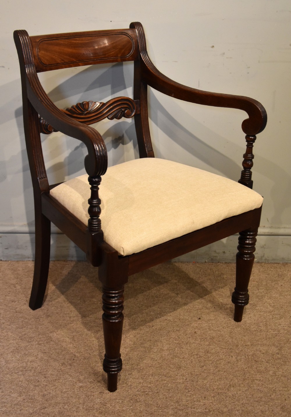 A Regency period mahogany open armchair featuring a reeded tablet top rail, carved scroll mid-rail, turned front legs, and cream fabric seat. View III