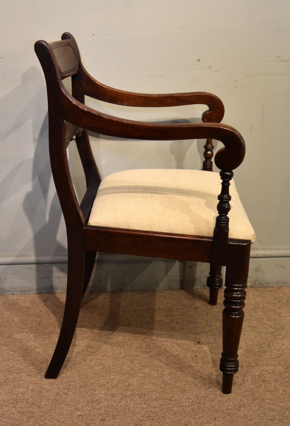 A Regency period mahogany open armchair featuring a reeded tablet top rail, carved scroll mid-rail, turned front legs, and cream fabric seat. View IV