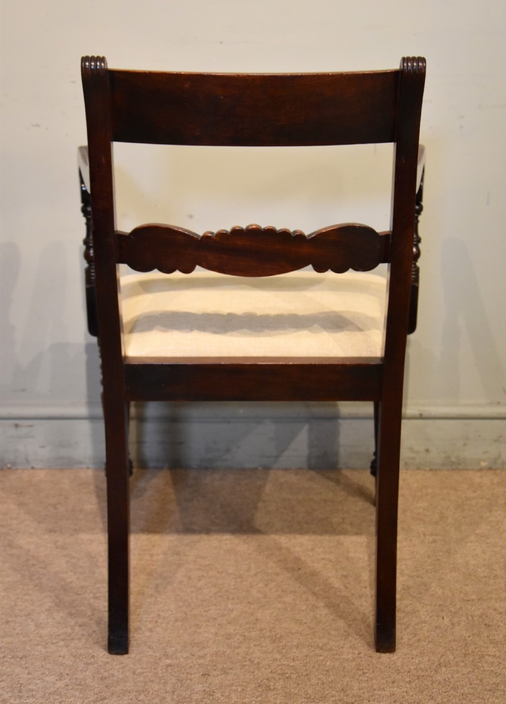 A Regency period mahogany open armchair featuring a reeded tablet top rail, carved scroll mid-rail, turned front legs, and cream fabric seat. View V