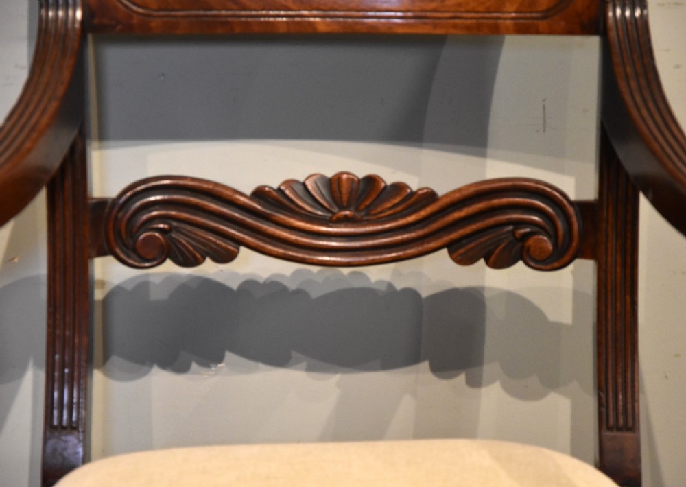 A Regency period mahogany open armchair featuring a reeded tablet top rail, carved scroll mid-rail, turned front legs, and cream fabric seat. View VI