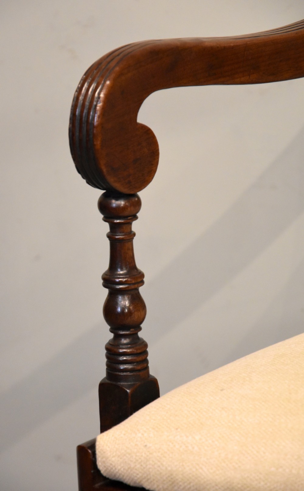 A Regency period mahogany open armchair featuring a reeded tablet top rail, carved scroll mid-rail, turned front legs, and cream fabric seat. View VII