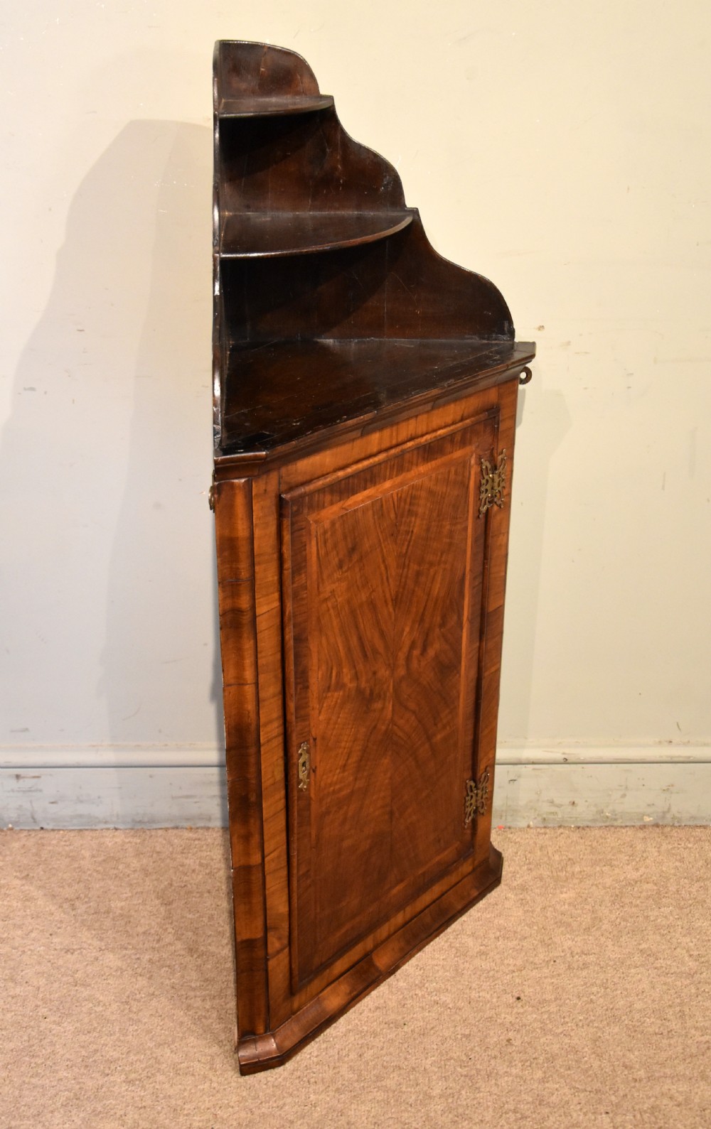 A George I walnut corner cupboard featuring a tiered open shelf superstructure above a panelled door with book-matched veneer and brass hinges. View III