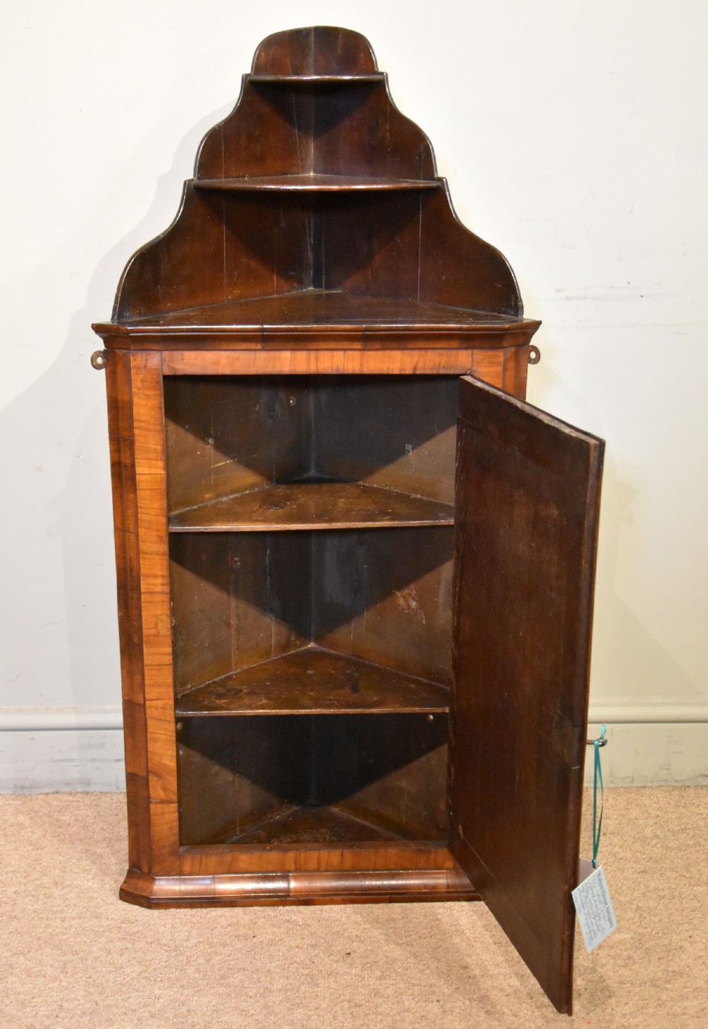A George I walnut corner cupboard featuring a tiered open shelf superstructure above a panelled door with book-matched veneer and brass hinges. View IV