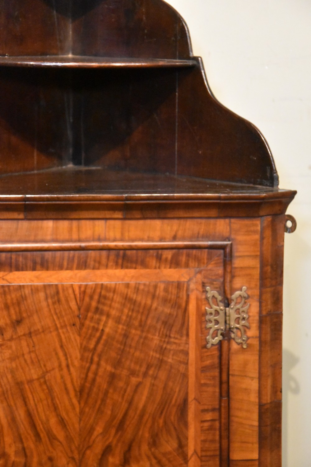 A George I walnut corner cupboard featuring a tiered open shelf superstructure above a panelled door with book-matched veneer and brass hinges. View VI