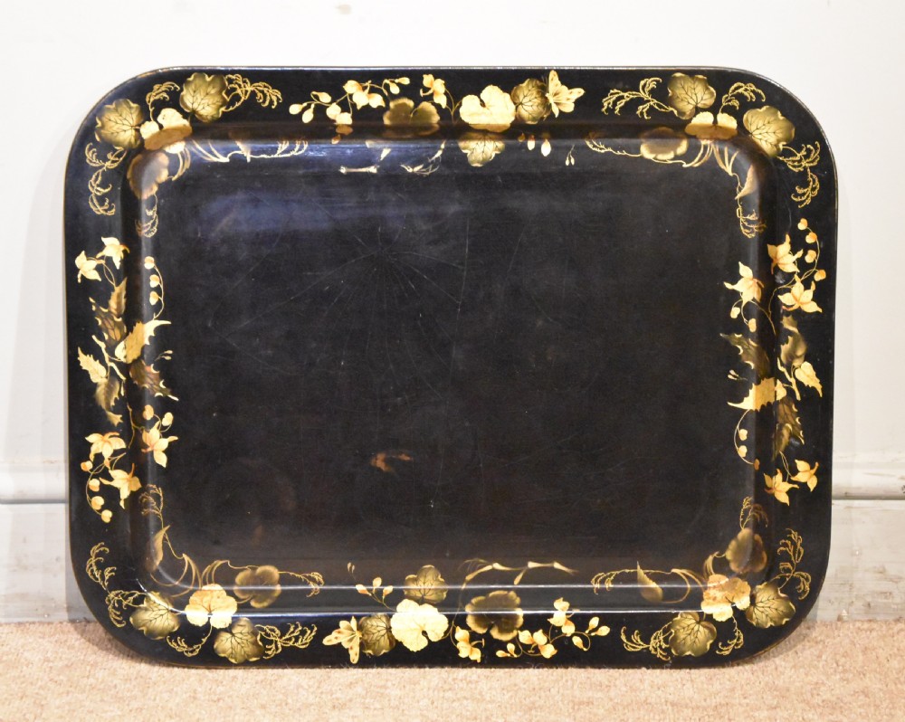 A large rectangular black lacquered Regency papier-mache tray decorated with gilt foliage along its raised rim.