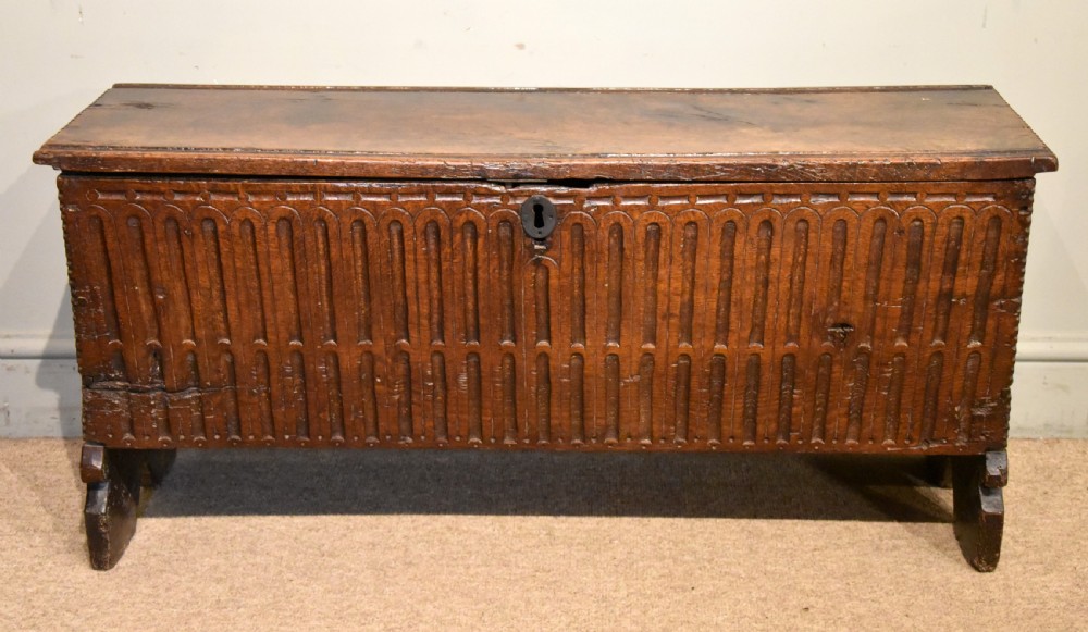 A sixteenth-century dark oak coffer featuring vertical fluted carvings across the front panel and a metal keyhole escutcheon.